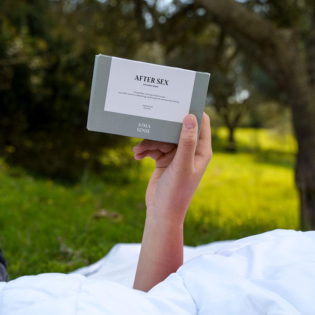 Hand håller Aima Sense After Sex intimwipes-förpackning i grönskande miljö